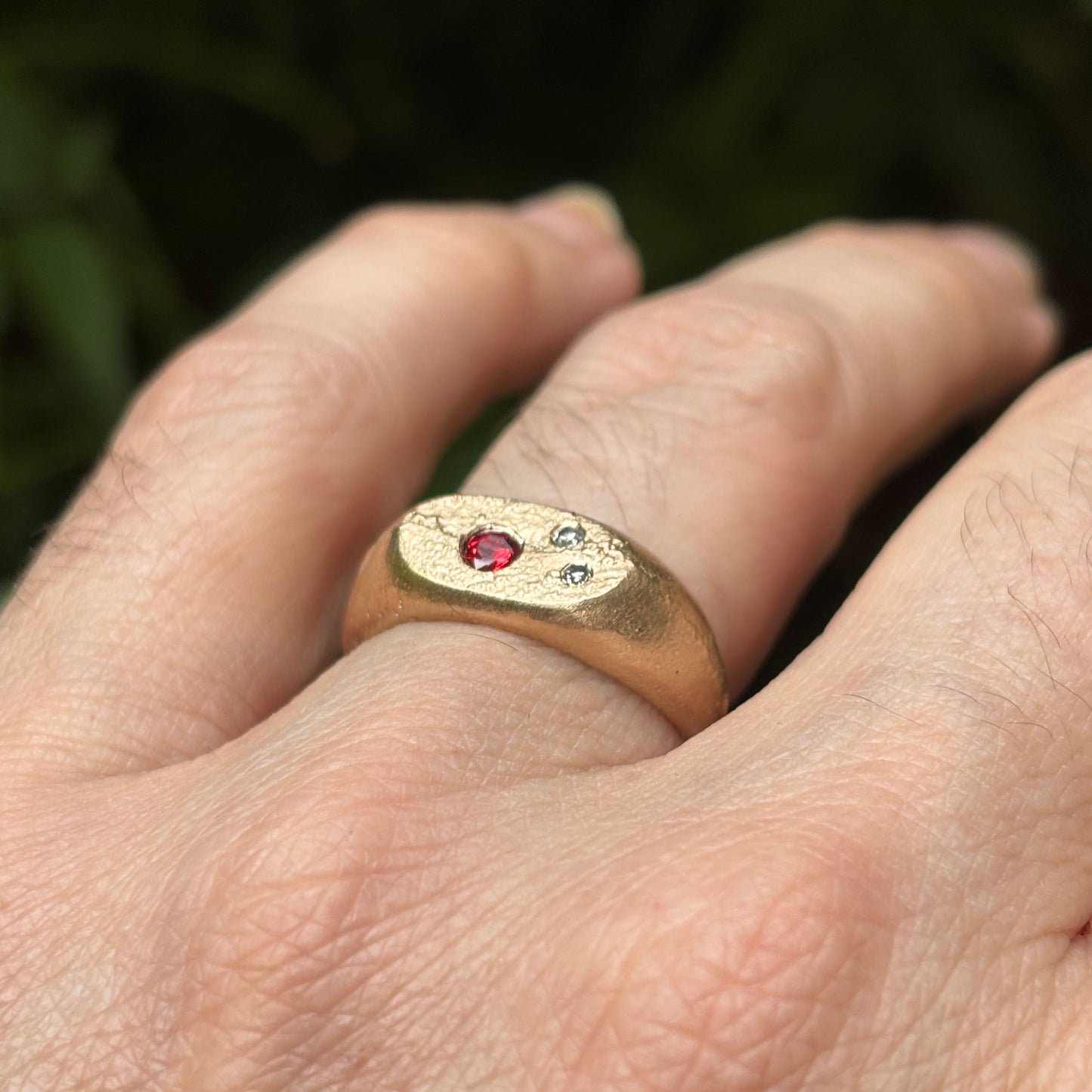 Gold ring with gemstones on a hand against a blurred natural background
