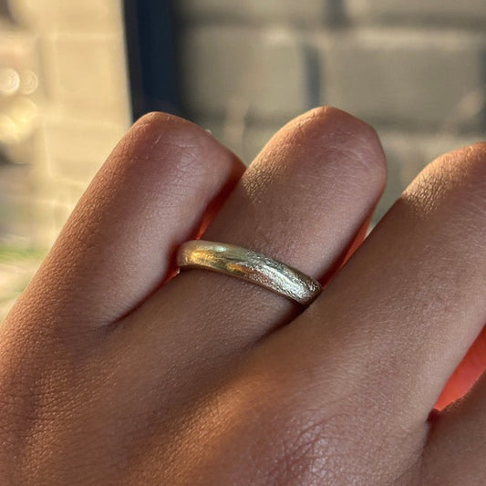 A close-up of a hand wearing a textured, hammered gold band ring.
