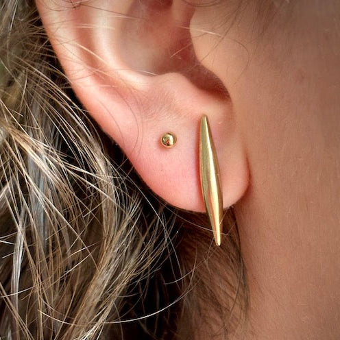 Close-up of an ear wearing a gold earring with hair partially visible.