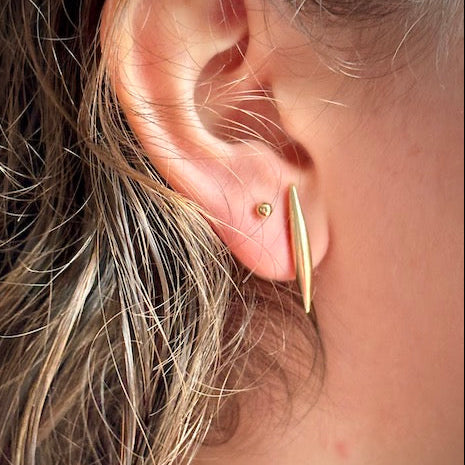Close-up of an ear wearing a gold earring with hair partially covering the frame.