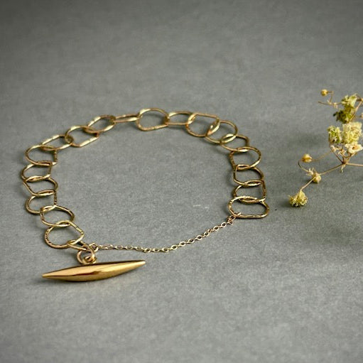 Gold chain bracelet with a small gold surfboard charm on a gray background