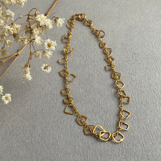 Gold chain necklace next to white flowers on a gray background