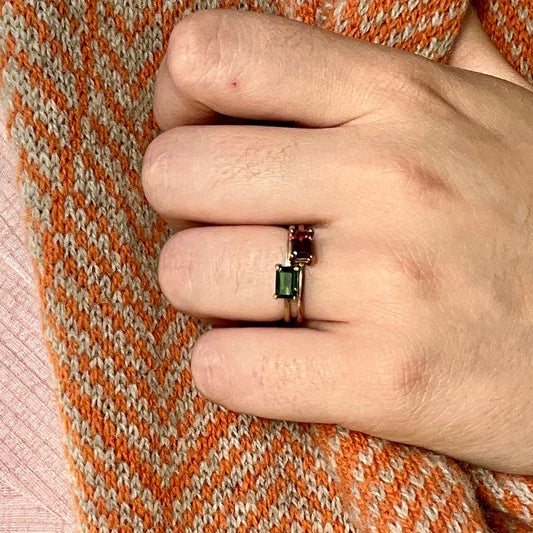 Hand wearing a ring with a green gemstone on an orange and beige patterned fabric background