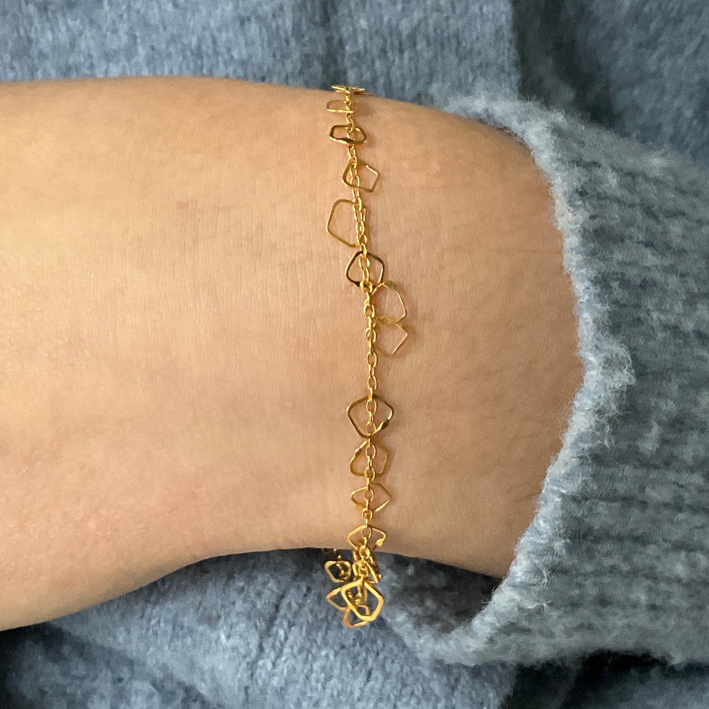 Gold bracelet on a wrist with a gray sleeve