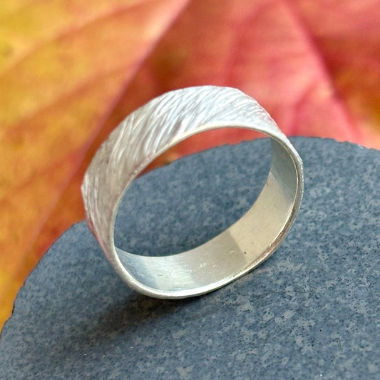 Silver ring with textured surface on a dark stone with a blurred red and yellow leaf background