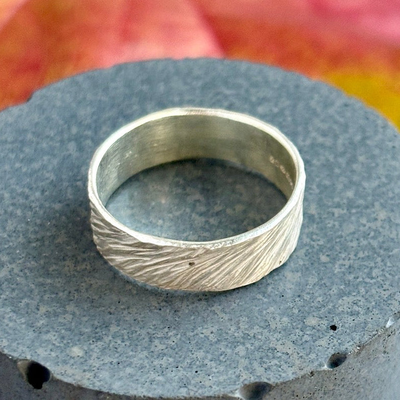 Silver ring with textured design on a gray surface