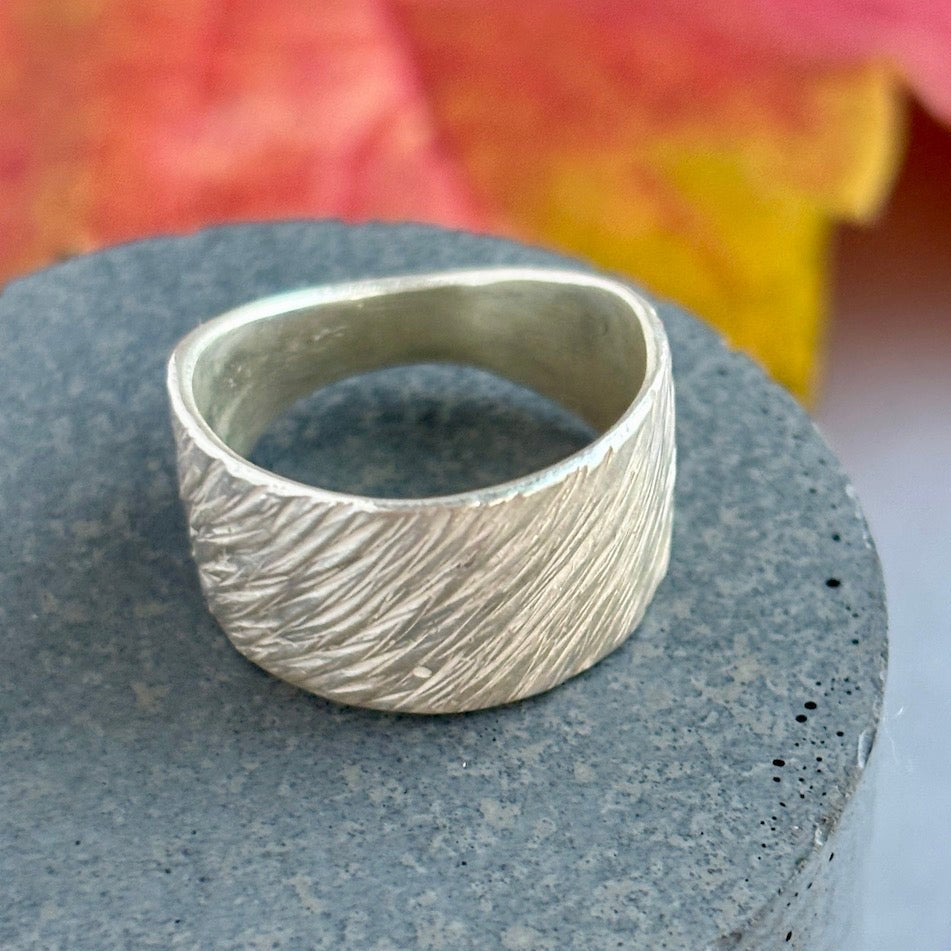 Silver ring on a textured gray surface with a blurred natural background