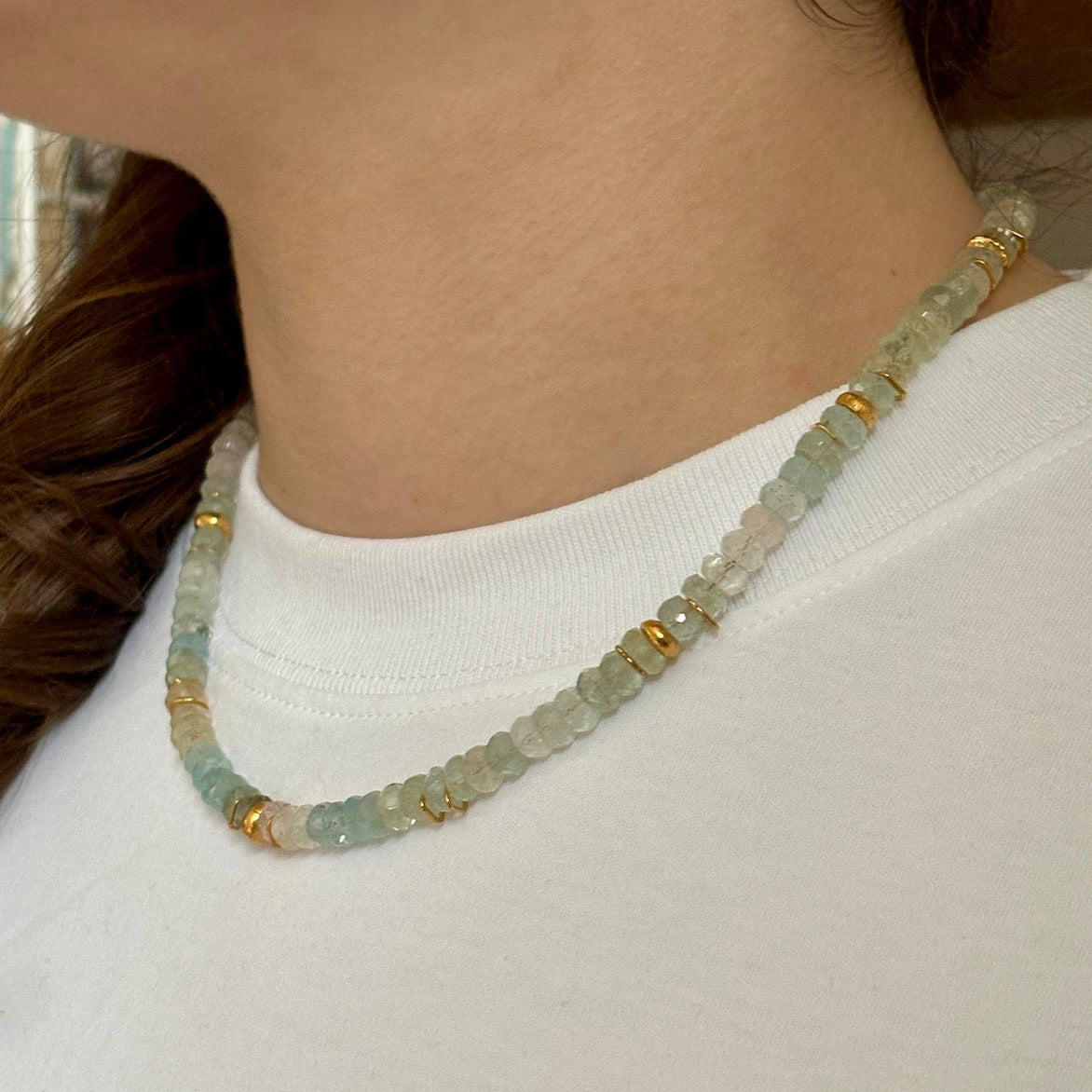 Necklace with green and gold beads worn by a person against a white background