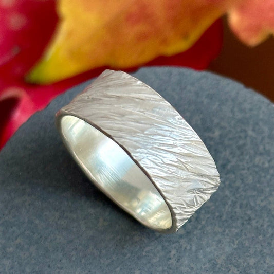 Silver ring with textured band on a gray surface with blurred colorful background