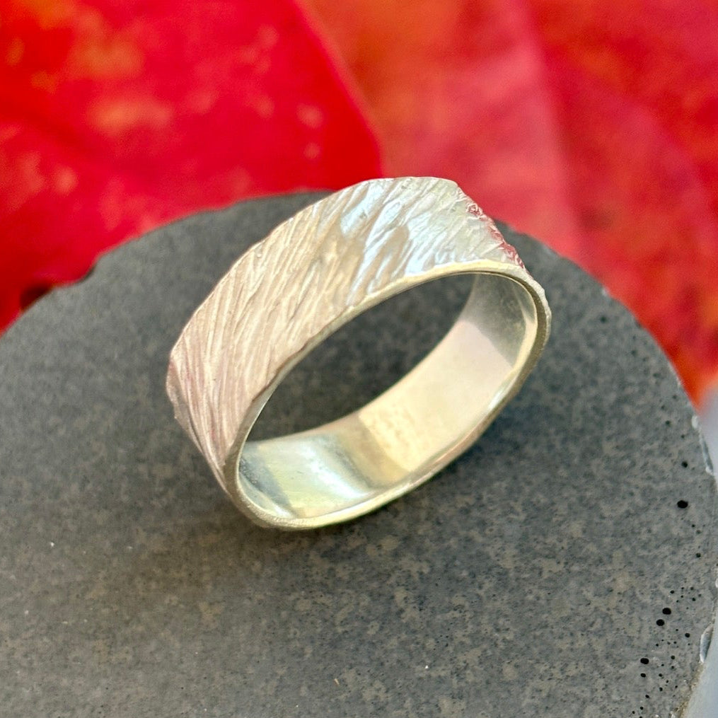 Silver ring with wavy texture on a dark surface with a red background