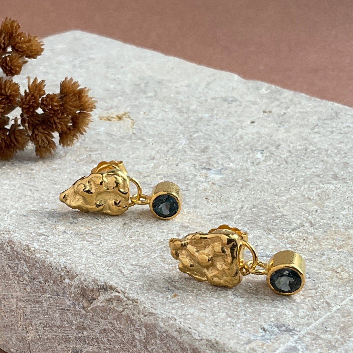 Gold earrings with black stones on a stone surface
