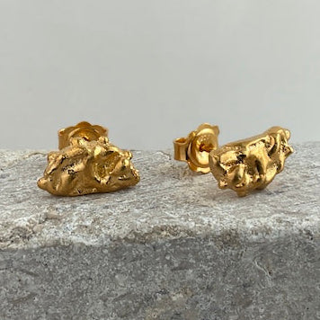Gold rock-shaped earrings on a gray surface
