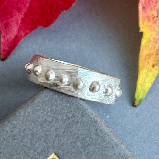 Silver ring with textured design on a gray surface with leaves