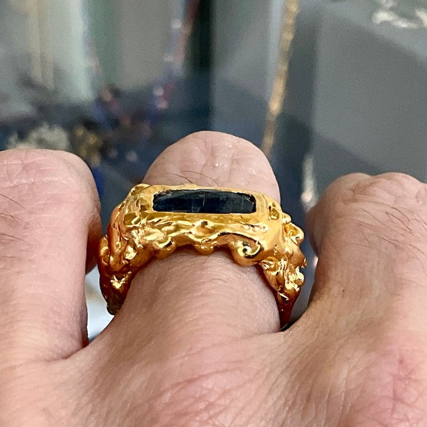 Gold ring with black stone held between fingers against a blurred background