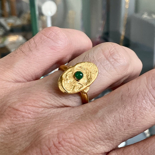 Gold ring with a green gemstone on a person's finger, blurred background