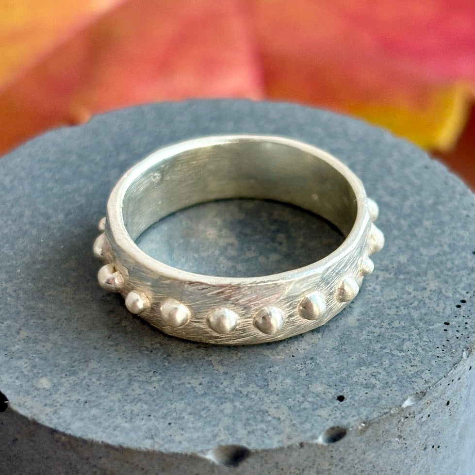 Silver ring with textured design on a gray cylindrical object with autumn leaves in the background