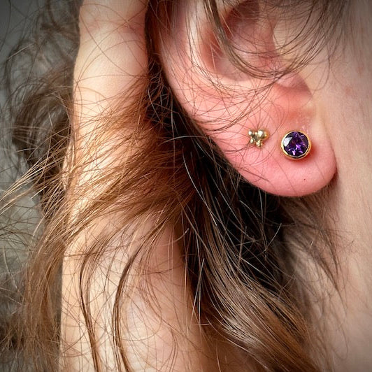 Close-up of an ear wearing two gold earrings with gemstones.