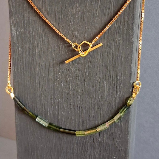 Gold necklace with green beads on a dark wooden surface