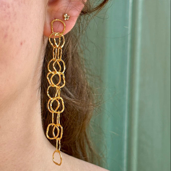 Gold chain earrings worn by a person with a teal background