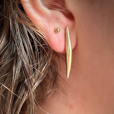 Close-up of an ear wearing a gold earring with a blurred background
