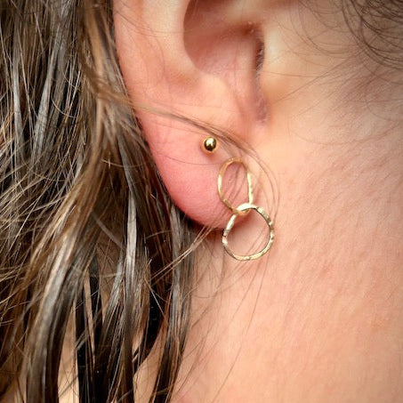 Close-up of a person wearing gold hoop earrings with a blurred background