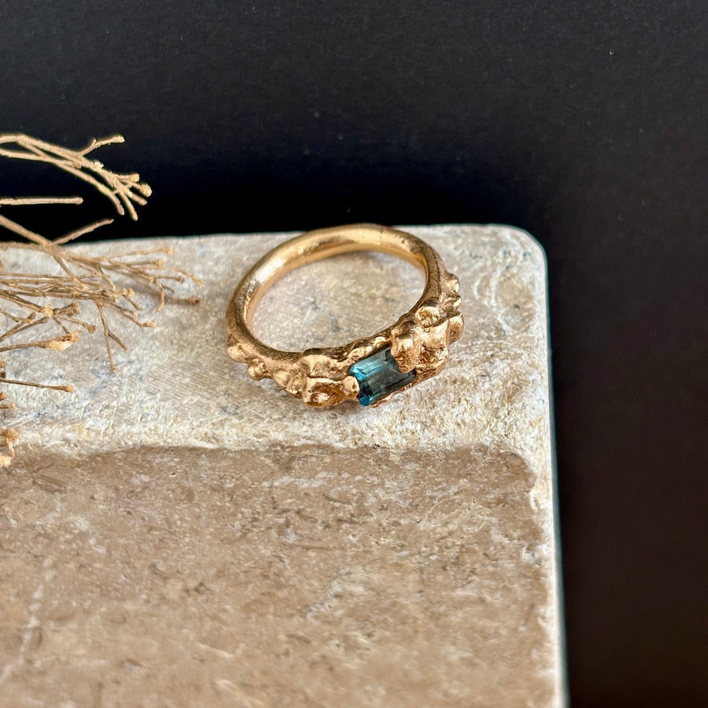 Gold ring with a blue gemstone on a stone surface with a dark background