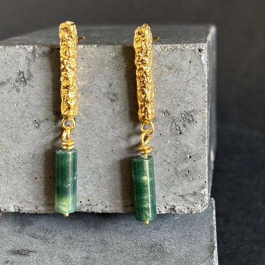 Gold and green earrings on a concrete block