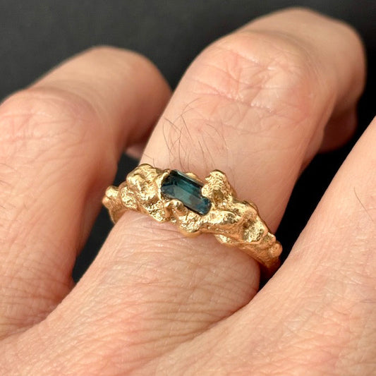 Gold ring with a central gemstone on a finger against a dark background