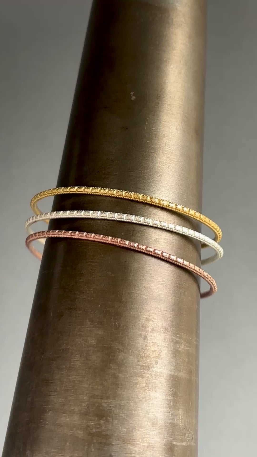 Bea Jareno Jewellery brand video. The Indian summer collection patterned bangles set in a mandrel top recycled 24ct yellow gold vermeil, middle recycled sterling silver and bottom recycled 24ct rose gold. Grey background 