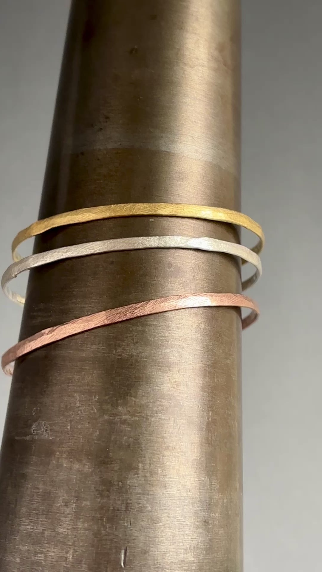 Bea Jareno Jewellery vídeo. Three Indian summer collection bangles with textures in a mandrel . Top recycled 24ct yellow gold vermeil, middle recycled sterling silver and bottom recycled 24ct rose gold vermeil . Grey background 