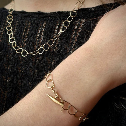 Gold chain bracelet on a wrist with a blurred black lace background