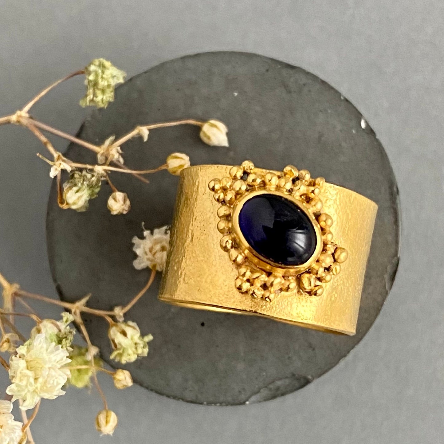 Gold ring with a dark gemstone on a gray background with dried flowers