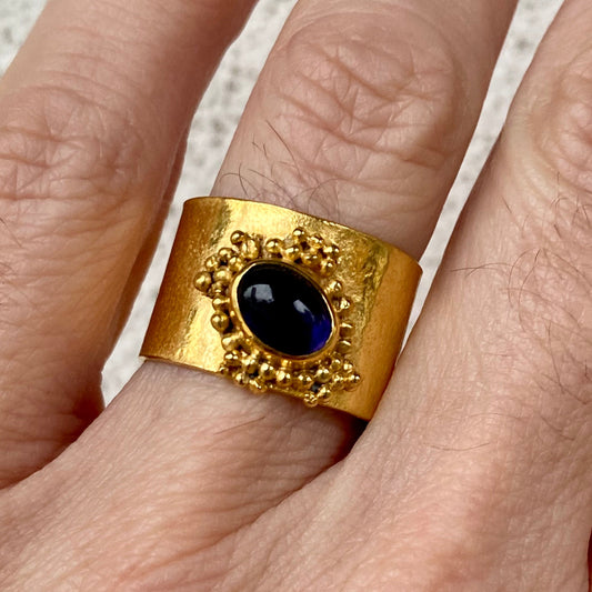 A gold-plated band ring with a central blue gemstone, surrounded by granulation details.