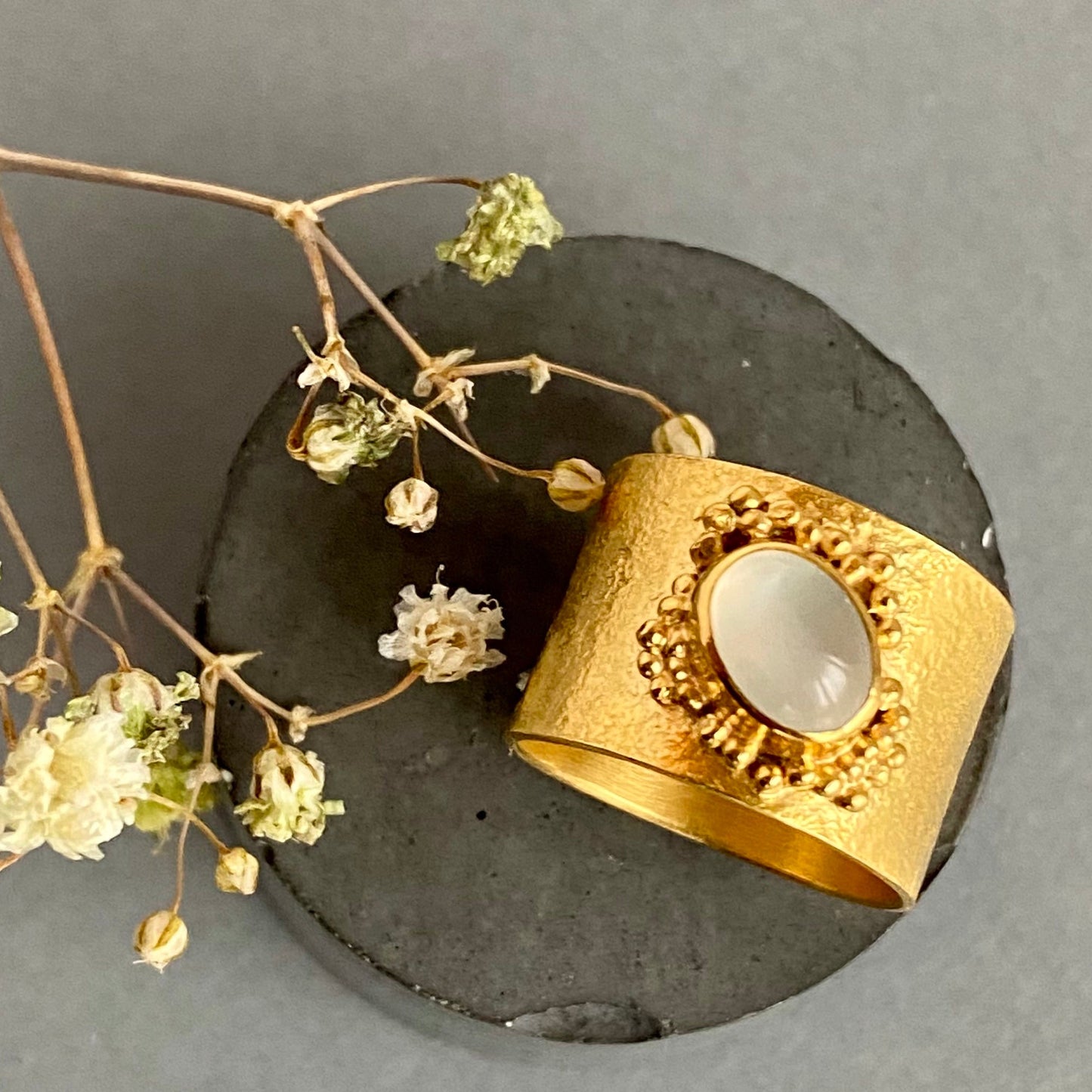 Gold ring with a stone on a dark surface with dried flowers