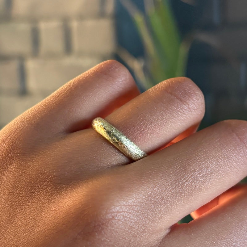 A close-up of a hand wearing a textured, hammered gold band ring.