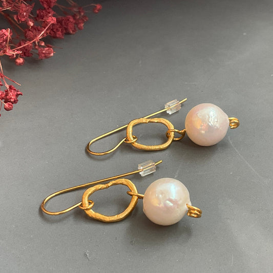 Pair of pearl earrings with gold hooks on a gray surface.