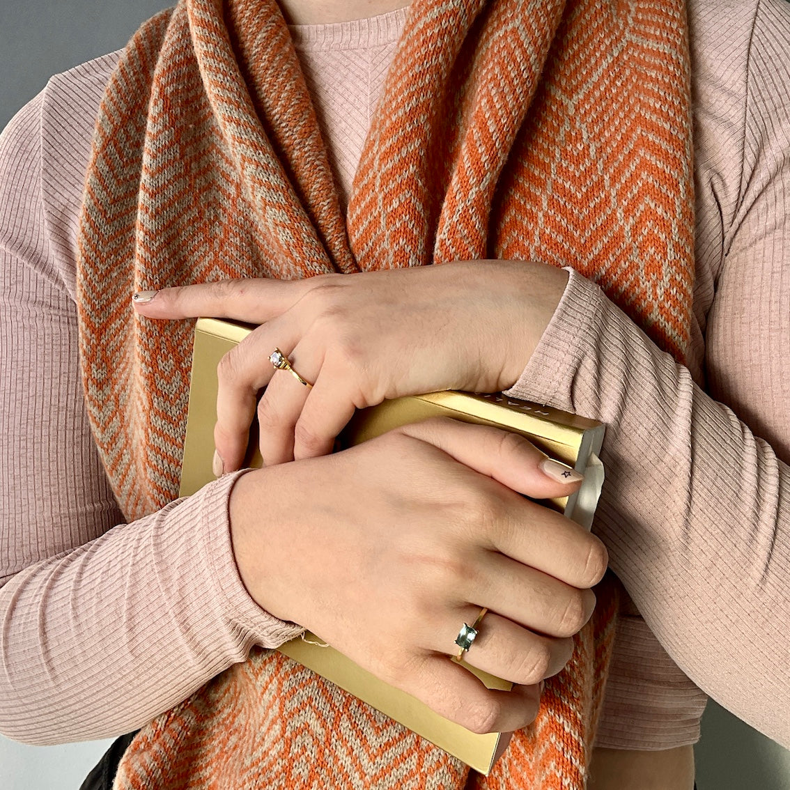 Bea Jareno Jewellery two recycled 18ct yellow gold rings modelled on hands by model holding a book grey background