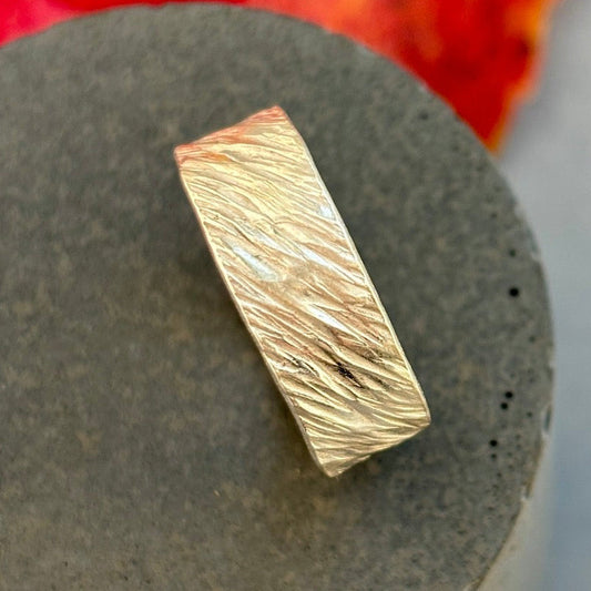 Gold ring with wavy pattern on a gray surface with red background