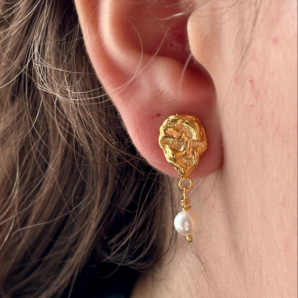 Gold earring with a pearl drop worn by a person