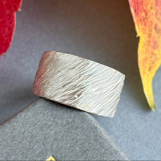 Silver ring with textured surface on a gray background with red and yellow leaves.