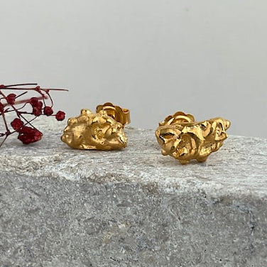 Gold textured earrings on a stone surface with a light gray background