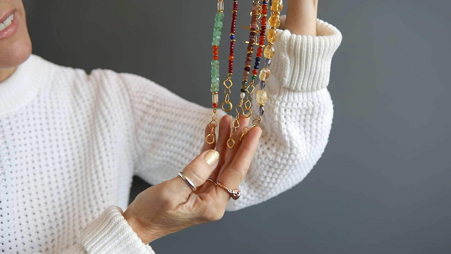 Founder, Bea Jareno, holding five necklaces from the Indian summer collection 24kt gold vermeil recycled with precious and semiprecious gemstones grey background