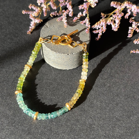 Green beaded bracelet with gold accents on a dark surface with decorative pink flowers.