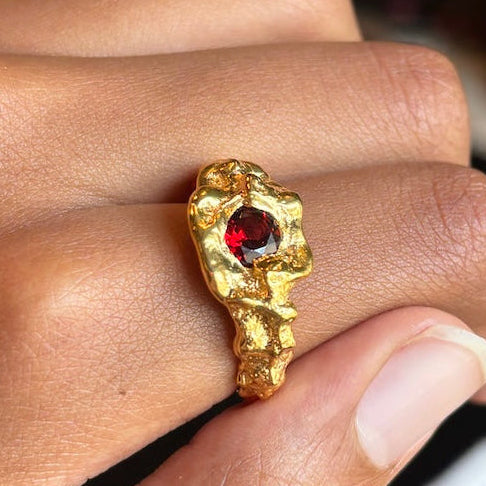 gold ring with garnet gemstone in a hand
