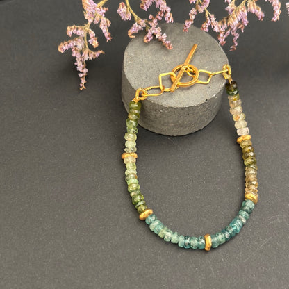 Beaded necklace with gold accents on a gray surface with decorative flowers.