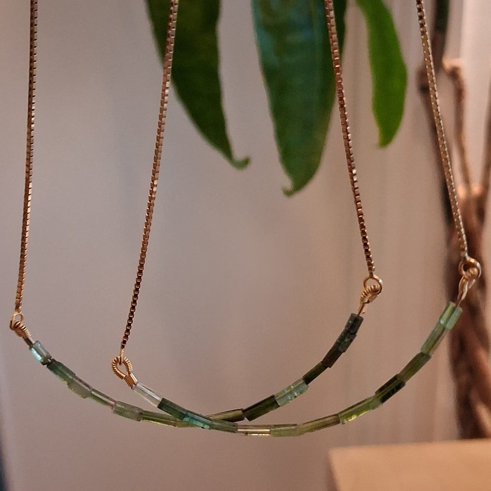 Necklace with green beads and gold chain against a blurred natural background