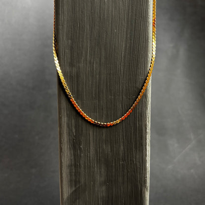 A gold chain necklace draped over a dark gray wooden display stand against a dark gray background.