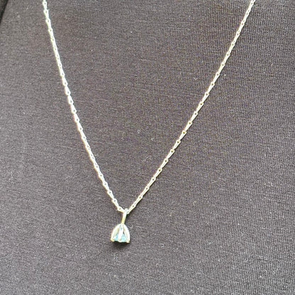A delicate silver chain necklace with a small teardrop-shaped pendant featuring a light blue iridescent stone, displayed on a textured dark gray fabric background.