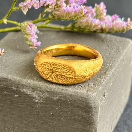 Gold ring with textured design on a stone surface with pink flowers in the background