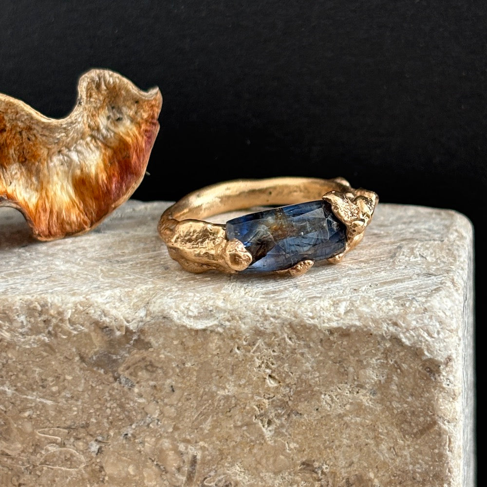 Gold ring with a blue stone on a stone surface with a dark background